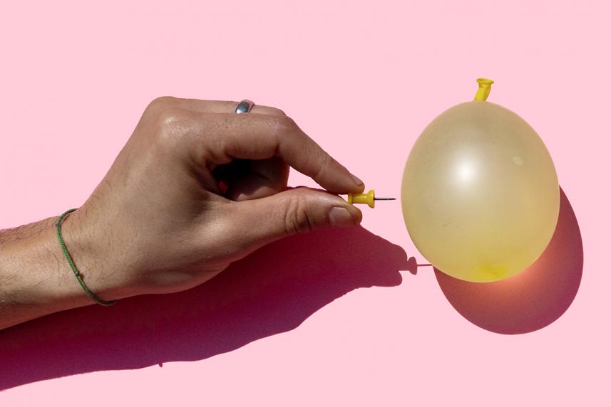 A hand holding a pin to a water balloon