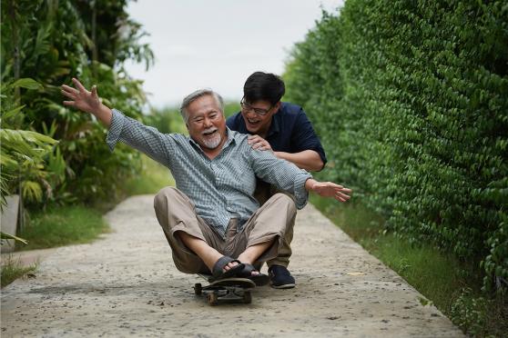 Father sitting on a skateboard and being pushed by his son