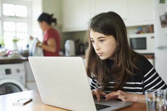 A pre-teen on her computer as her mother finishes the dishes. 
